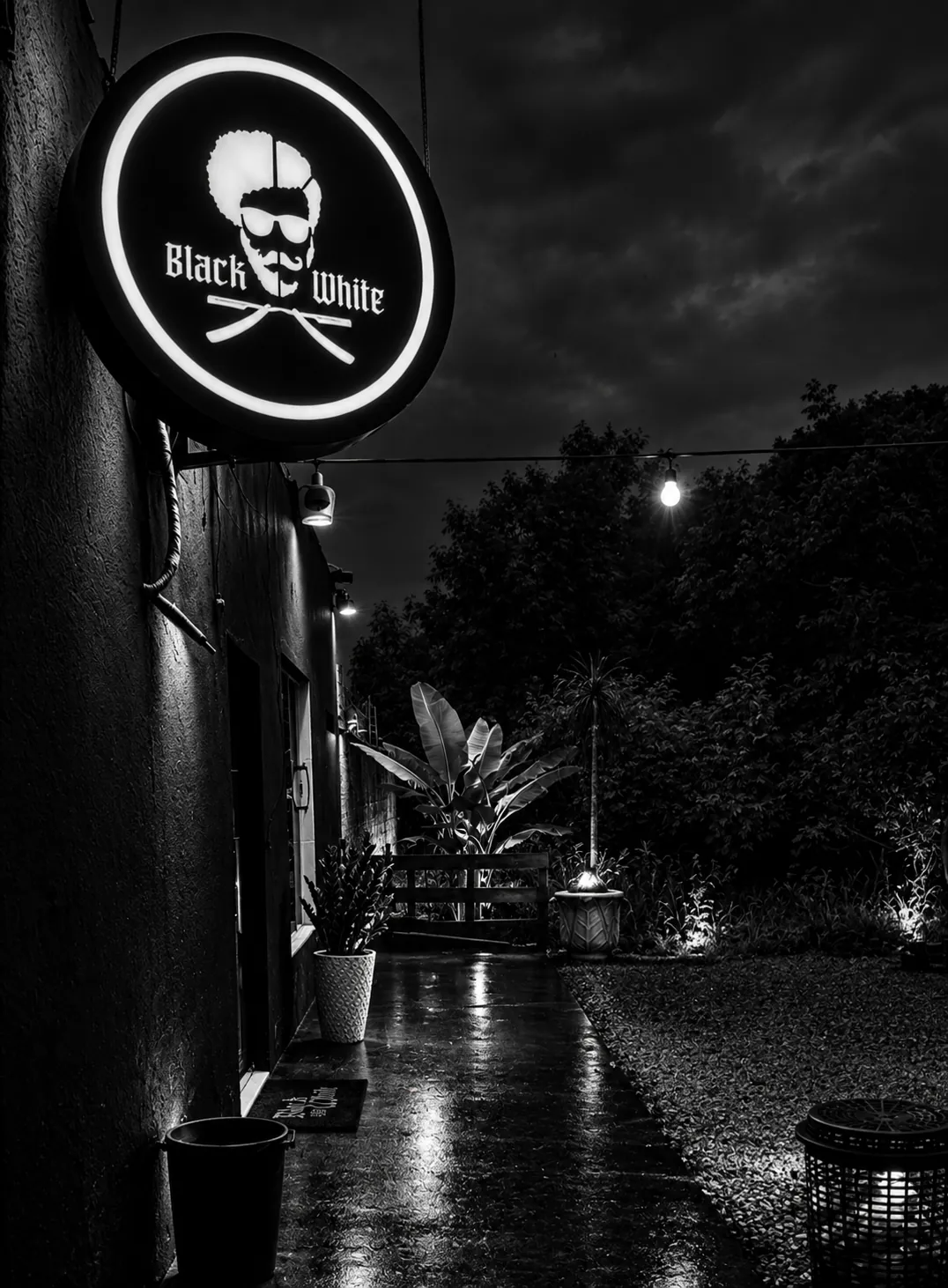 Fachada da Barbearia Black White à noite, com o letreiro circular iluminado — capa oficial do site